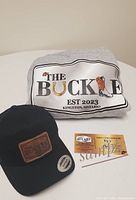 Photo showing grey hoodie with The Buckle logo, black ballcap with leather patch, and a $25 gift card for The Buckle.