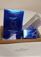 Photo showing boxed Zo Skin Health wrinkle + texture repair face creme (30ml), exfoliating polish (16.2g), two white headbands with blue printed logo, all presented on a surface with The Refinery logo.