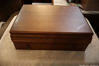 Closed wooden flatware box showing carved leaf design trim and metal ring handles