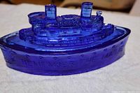 Side view of cobalt blue glass candy dish showing ship design and embossed "Remember the Maine" text