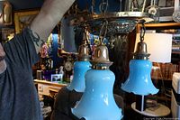 Photo showing the entire fixture with three blue glass shades hanging down, bronze finish, fixture held up by a person.