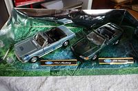 Two diecast Mustang models on scenic green base, showing both cars and Ford brand nameplates for 1964 and 1998.