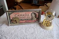 Photo showing both clocks together on a white surface; left is Canada $1000 bill clock, right is anniversary dome clock.