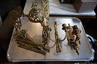 Three antique light fixtures laid on a metal tray, showing detailed ornate design and metal finishes.