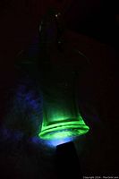 Uranium glass basket glowing green under UV light, showing translucent detail and handle