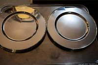 Top view of two silver plated charger plates showing the reflective surface and rim detail, placed on a metallic surface.