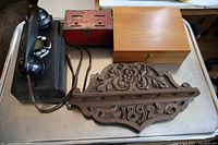 Black Northern Electric wall phone, red metal slot box, wooden locked box, and carved 1892 wooden pipe holder photographed on metal surface.