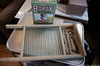 Overview of the wooden frame Economy washboard with glass ridged scrubbing surface alongside a vintage Borax laundry soap box on a metal tray.
