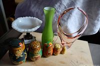Full front view of all items in the lot displayed on table including pink art glass sculpture, green vase, milk glass candy dish, and five hand-painted bear nesting dolls arranged in size order.