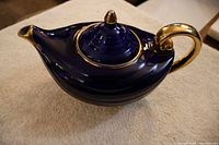 Side angle of cobalt blue ceramic tea pot shaped like an Aladdin lamp with gold-trimmed handle and spout.
