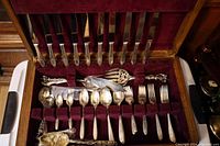 Open cutlery case showing the full set of Oneida Grosvenor silver-plated cutlery including knives, forks, spoons, serving forks, serving spoons and specialty pieces arranged in red velvet lining.