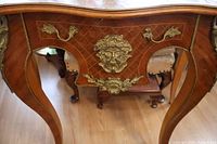 Close-up view of the front of the console table showing the wood veneer with diamond inlay pattern and ornate brass ormalou decorations including a face motif and floral mounts.