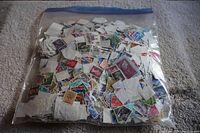 Plastic bag filled with many used postage stamps from Great Britain, showing varied colors, designs, and many duplicates.