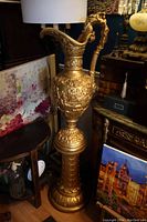 Full view of the large gold painted ewer on its stand showing its height and placement in a room.