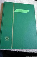 Closed green stock book with gold vertical stripe and emblem, labeled "Belgium Stamps" on green tape