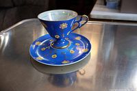 Old Japanese teacup with saucer, blue with floral pattern and gold accents on silver table.