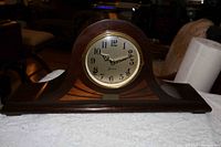 Front view of the wooden Sessions mantle clock on a white surface, showing the full cabinet and clock face with inlay decoration on the base.