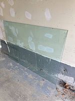 Rectangular clear tempered glass table top leaning against a wall on floor, showing chip on corner.