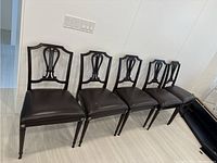 Front view of all five chairs lined up, showing espresso leather seats and dark wood frames with decorative backs and tapered legs.