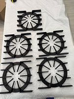 Top view showing five black cast iron spider-style grates arranged in two rows on a white surface.