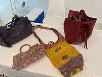 Four assorted purses arranged on a white surface including burgundy tote, purple sequin handbag, patchwork yellow-green-purple hobo, and snakeskin clutch