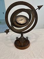 Front perspective of a decorative compass holding a battery operated clock with ornate metal rings and wooden base.