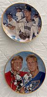 Photo showing two collectible plates: one featuring Ken Griffey Jr. in Mariners baseball uniform, the other showing hockey players Bobby and Brett Hull in their team uniforms, both showing signatures.