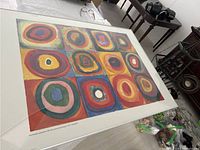 Photo showing the entire large Kandinsky poster with visible cracks in the glass frame on a floor with surrounding objects.