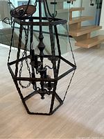 Full view of the large wrought iron hanging light fixture showing the rectangular twisted bar frame and six candle-style bulbs inside.