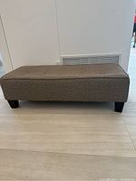 Side view of rectangular fabric bench showing fabric texture and wooden legs.
