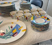 Full view of stacked plates, cups, and saucers showcasing colorful floral abstract design and silver rim detail.