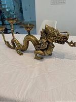 Side view of ornate brass dragon candle holder showing detailed textured scales, feet, crown, and three candle holders on back.