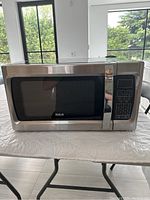Full view of the black and stainless steel microwave oven on a white surface, showing the door with the RCA logo.