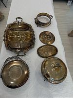 Photo showing all silver plated serving pieces laid out on a table, including trays, cake plate, covered dish, and holders. Tarnished surfaces visible.
