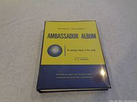 Front cover of the Ambassador stamp album, yellow and blue hardcover with globe image, labeled 'Ambassador Album' and 'for postage stamps of the world' copyrighted by H.E. Harris Co. 1963.