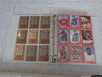 Open binder display of 9 hockey cards on the right side in clear protective sleeves showing front of cards with player images and red borders. The back of cards on left side show player stats and info with brownish design and text.
