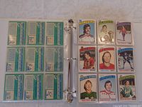 Binder page showing nine 1976-77 O-Pee-Chee hockey cards including Rangers, Islanders, Canadiens, Black Hawks, Red Wings, Penguins, North Stars, Capitals, Barons.