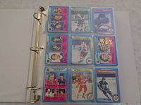 Photo of open binder showing 9 hockey cards in clear protective sleeves with front and back view showing player images and stats respectively.