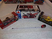 Three collectible die cast pickup trucks in original packaging displayed on a table with a tape measure for scale.