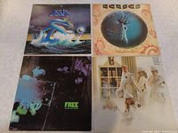 Four vinyl LP records from rock bands Asia, Free, Kansas, and Cheap Trick laid out on surface showing album cover art for each.