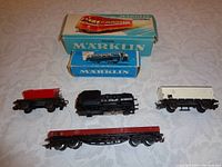 Top view photo of all six Marklin model train pieces with two original boxes shown behind them on a beige surface