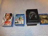 Four stacks of DVD and Blu-ray TV series including Dexter, Breaking Bad, Game of Thrones, The Walking Dead placed on white patterned surface