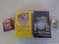 Four unopened cardboard boxes of football card sets and a sealed set of cards, laid on a beige fabric surface.