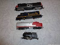 Four HO scale model train engines displayed from top CN diesel black and silver, blue Santa Fe diesel, silver and red Santa Fe diesel, to bottom black New York Central steam engine.