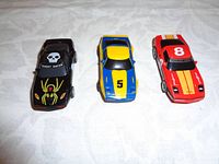 Three HO scale slot cars: black 'Ghost Racer' car with spider graphic, blue/yellow car #5, red car #8 with stripes