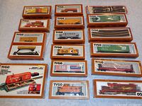 Overview of all 15 pieces in original Tyco boxes with orange trim and clear window display, showing various freight cars and track pieces.