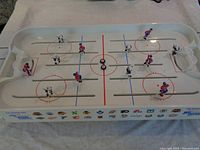 Overhead view of the Wayne Gretzky Overtime Hockey Game showing red and blue players on metal rods, rink markings, and one of the white plastic goal nets.