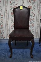 Front view photo of antique leather detailed chair showing leather seat and backrest with wooden carved legs and claw feet.