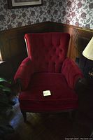 Photo of an antique armchair with red velvet upholstery and tufted backrest in a corner setting.