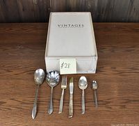 Six pieces of assorted flatware laid out in front of a white closed box marked Vintages.
